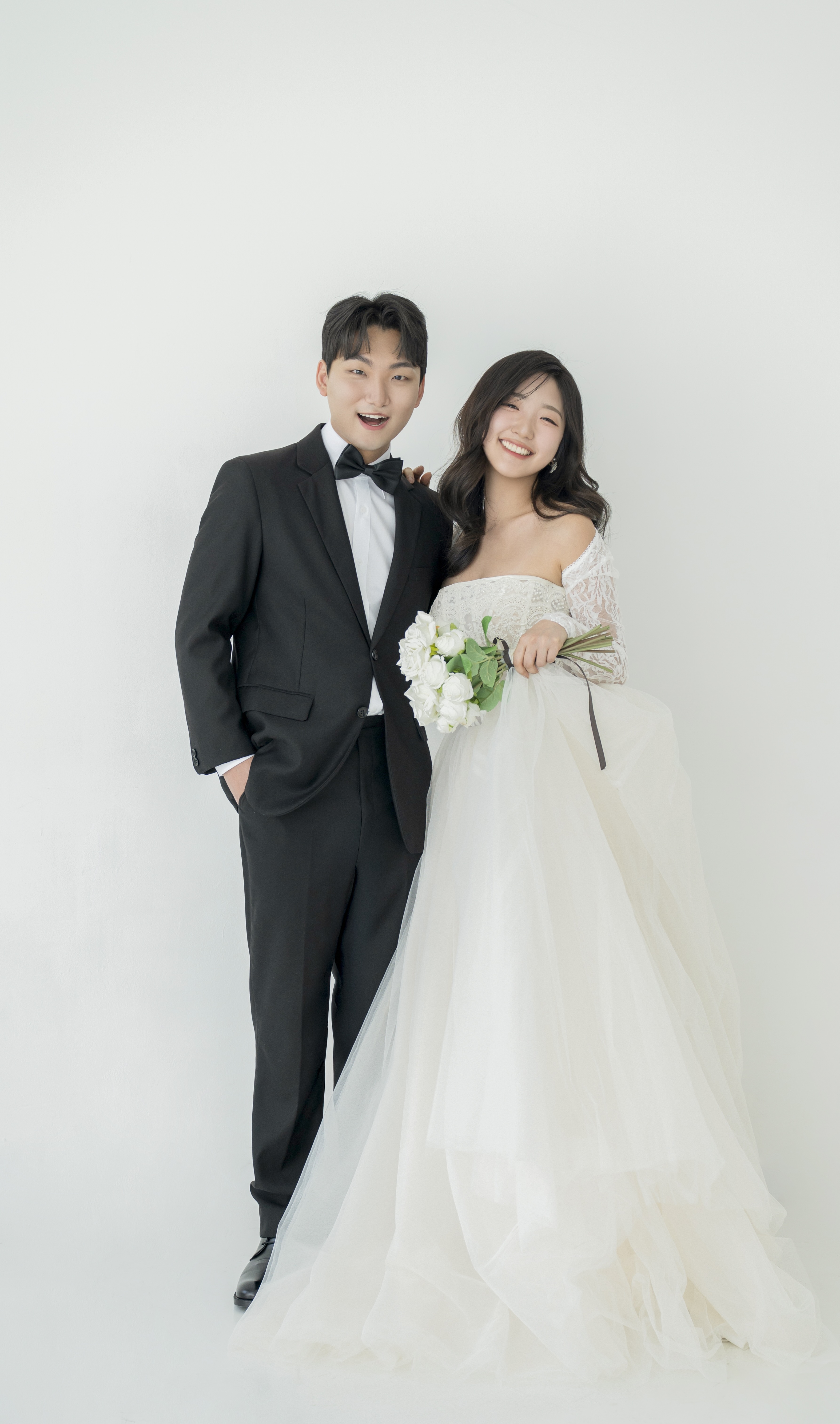 흰 배경 앞에 서 있는 서병준과 백소현의 웨딩 사진